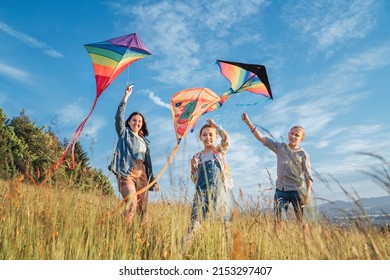 Smiling gils and brother boy running with flying colorful kites on the high grass meadow in the mountain fields. Happy childhood moments or outdoor time spending concept image.