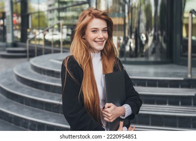 Smiling Ginger Business Woman With Laptop In Her Hands Smiling At Camera Standing Outside Office Building During Her Lunch Break. Outside During Break. Business