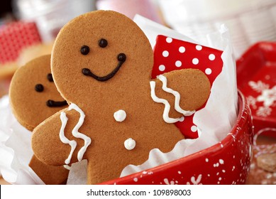 Smiling gingerbread men nestled in holiday dish with gift-wrapped surprise.  Baking ingredients and supplies (including baker's twine and rolling pin) in background.  Macro with extremely shallow dof.