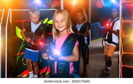 Smiling Girl Aiming Laser Gun At Other Players During Lasertag Game In Dark Room. High Quality Photo