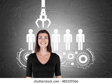 Smiling girl in black standing against chalkboard with conveyor belt of people. Concept of HR policy and the right candidate picking. 