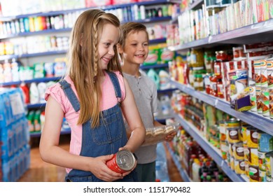 Smiling girl and boy choosing preserved meal for home in the supermarket