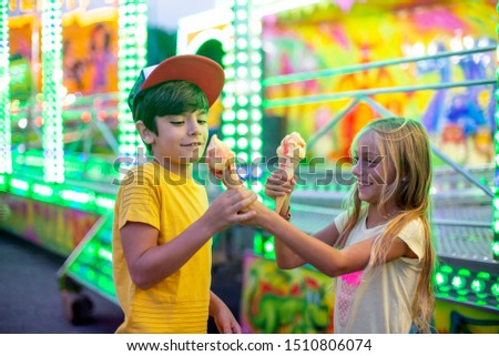 Smiling girl and boy eating ice cream in Funfair Park lights carnival
