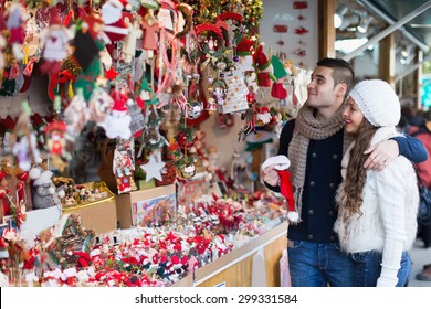 Smiling girl with boyfriend choosing Christmas decoration at fair. Focus on woman