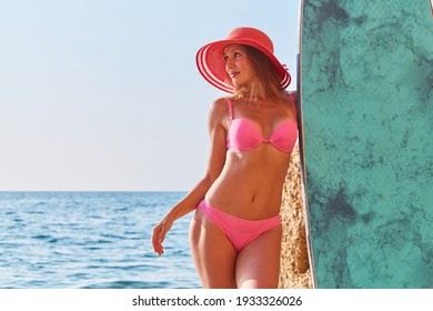Smiling girl in bright bikini on beach. Summer holidays and surfing idea. Cute woman posing with surfboard on seashore.