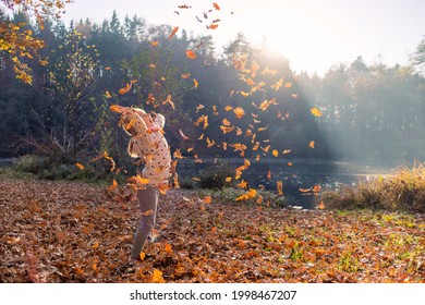 Smiling girl child throwing dry leaves in the air at beautiful autumn sunset.