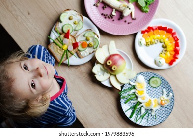 Smiling Girl With Colorful Funny Food On A Plate On A Table. Kids Food With Creative Form For Lunch Or Breakfast. Decorated Vegetables, Egg And Sandwich. Top View.