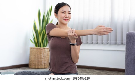 A smiling girl doing Deltoid Stretch for her shoulders exercising as her indoor leisure.