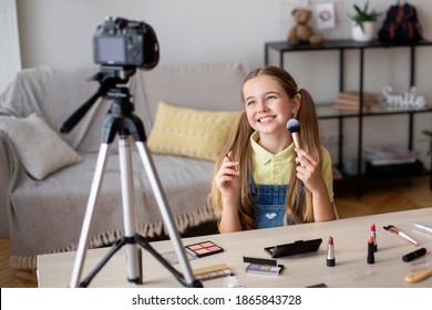 Smiling girl doing makeup, recording cosmetics product review, showing her brushes and make up for teens and yong skin, looking at camera on tripod. Girl filming video for her internet channel