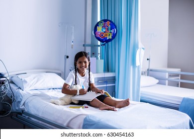 Smiling girl drawing picture in a book while sitting on hospital bed  - Powered by Shutterstock