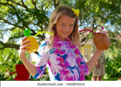 Smiling Girl Dressed Up For A Hawaiian Luau, Wearing A Flower Dress And Holding Tropical Drinks