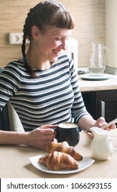 A smiling girl drinks coffee with a croissant and dials a message in the smartphone. - Shutterstock ID 1066293155