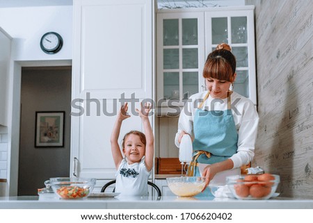 A smiling girl is happy as her mother whips up the dough with a mixer
