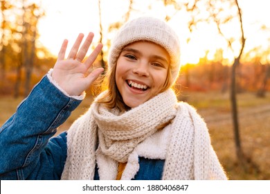 Smiling Girl In Knitted Hat And Scarf Walking In The Autumn Park, Waving Hand