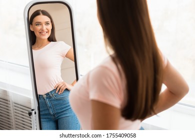 Smiling Girl Looking At Mirror After Slimming Happy About Dieting Result Standing Indoors. Weight Loss. Selective Focus