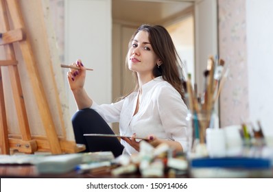 Smiling girl paints on canvas with oil colors in workshop