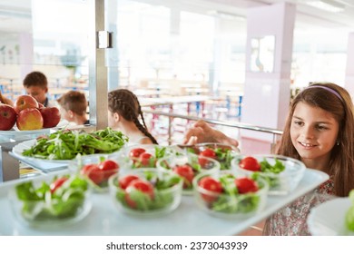 Smiling girl picking up vegetable salad during lunch time in school cafe