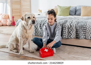 smiling girl playing doctor with toy first aid kit and labrador dog on floor in bedroom - Powered by Shutterstock