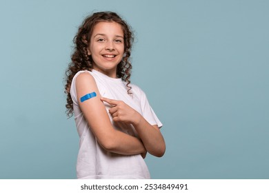 Smiling girl pointing at a blue bandage on her arm after receiving a vaccine. - Powered by Shutterstock