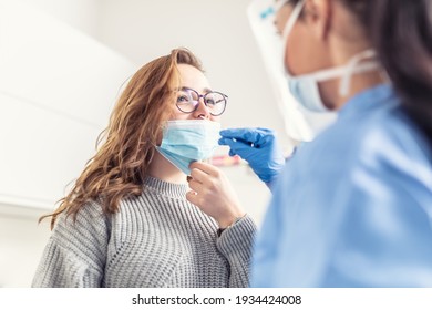 Lächelnde Mädchen legt ihr die Gesichtsmaske von der Nase ab, sodass ein medizinisches Fachpersonal eine Probe für Covid-19-Tests entnehmen kann.