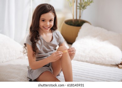 Smiling Girl Putting Band Aid On Knee At Home