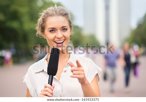 A smiling girl reporter with microphone in hand on\
the street