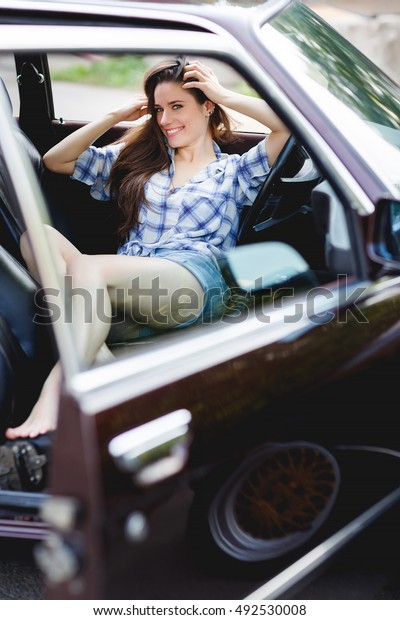 Smiling\
girl in short shorts in open car, tinted\
photo