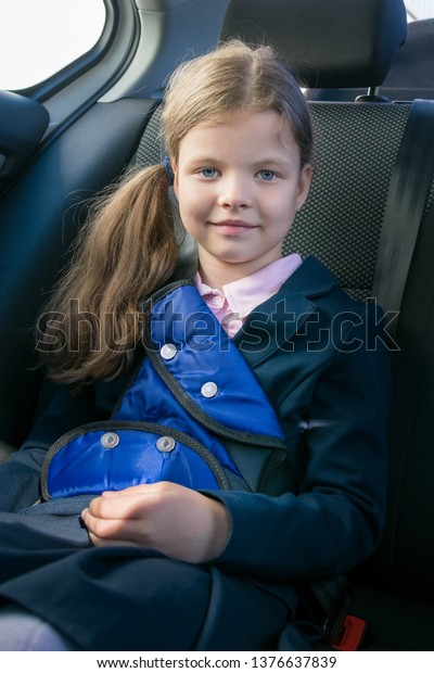 smiling girl sitting in a car wearing a seat belt in\
a child seat