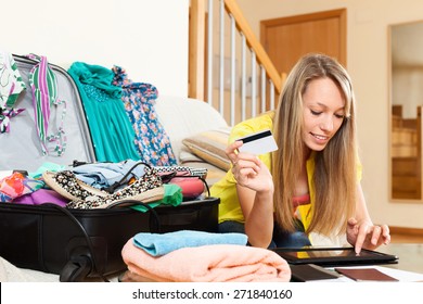 Smiling girl sitting near trunk with credit card and tablet at home