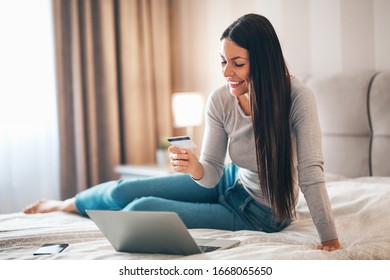 Lächelndes Mädchen sitzend auf dem Bett mit Laptop, während Sie Kreditkarte und überprüfen Sie Online-Shopping-Informationen.
