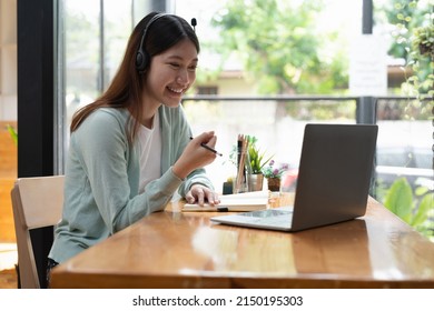 Smiling girl student wear wireless headphone study online with teacher, happy young asian woman learn language listen lecture watch webinar write notes look at laptop sit in cafe, distant education