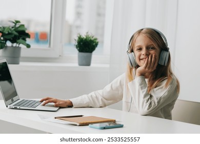 Smiling girl studying at home with a laptop for elearning She is sitting at a table, absorbed in her online lesson, surrounded by books and school supplies With headphones on, she is fully engaged, - Powered by Shutterstock