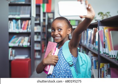 Smiling girl taking selfie while standing by bookshelf in library - Shutterstock ID 680195275