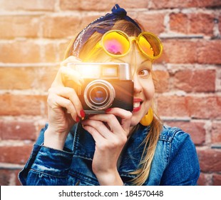 smiling girl with vintage camera taking photo with flash on brick wall background
