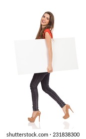 Smiling Girl Walking With Blank Placard Holding Under Her Arm. Full Length Studio Shot Isolated On White.