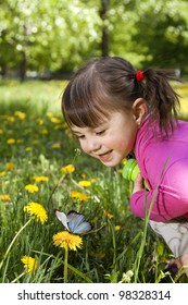 A smiling girl wearing a pink shirt, sitting on the dandelion field and observing a butterfly