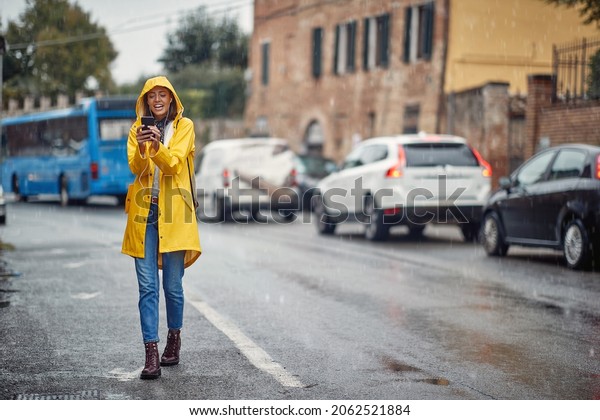 Smiling girl in a yellow raincoat listens to music\
and walks in the rain