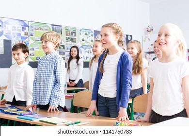 Smiling Girls And Boys Singing Song In The Classroom During Music Lesson