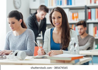 Smiling girls sitting at desk and studying in the classroom, learning and education concept - Powered by Shutterstock