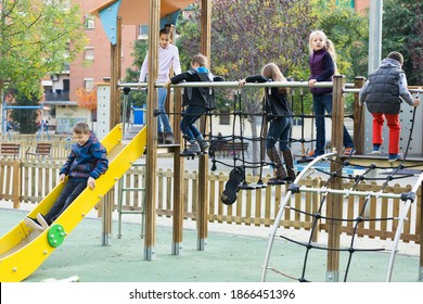 Smiling Glad Kids In School Age Sliding Down Together On Playground's Construction Outdoors