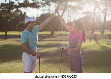 Smiling golf player couple giving high five while standing on field - Powered by Shutterstock