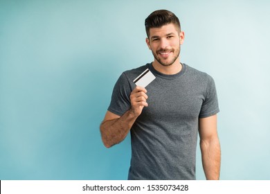 Smiling Good Looking Man Holding Credit Card While Making Eye Contact  In Studio