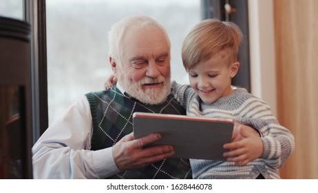 Smiling Grandfather And Grandson Using Digital Tablet For Surfing Internet And Playing Game Near The Fireplace At Home Grandpa Adult Grandchild Child Childhood Communication Computer