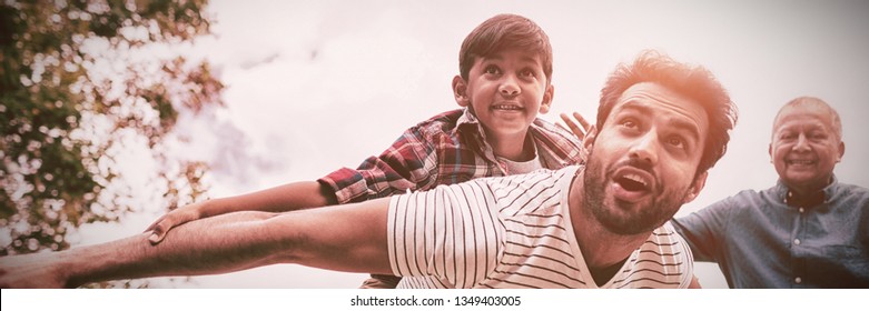 Smiling grandfather looking at man giving piggy backing to son with arms oustretched in yard - Powered by Shutterstock