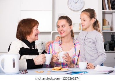 Smiling grandmother, mother and granddaughter drinking tea at home