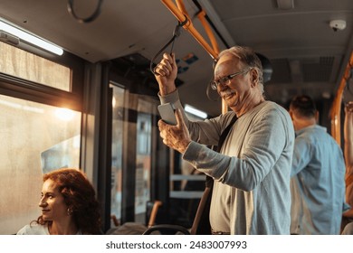 Smiling grandpa looking at his smartphone with a smile while he is standing inside a public bus holding onto a handrail. - Powered by Shutterstock