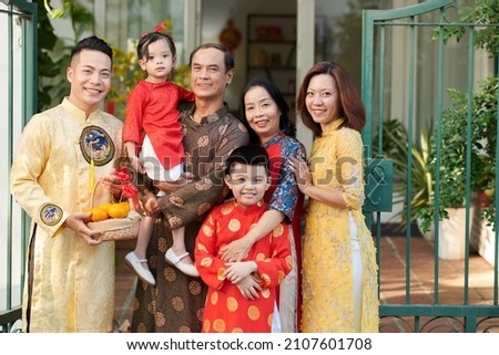 Smiling grandparents, parents and children in traditional ao dai dresses standing in front of house ready for tet celebration