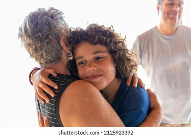 Smiling Grandson Gets Hug From Grandma, Dad In Blurred Background, White Background