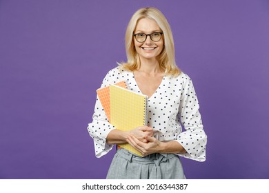 Smiling Gray-haired Blonde Teacher Woman Lady 40s 50s Years Old Wearing White Dotted Blouse Eyeglasses Standing Hold Notepads Looking Camera Isolated On Bright Violet Color Background Studio Portrait