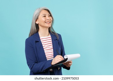 Smiling gray-haired business woman in blue suit isolated on blue wall background studio portrait. Achievement career wealth business concept. Mock up copy space. Hold clipboard with papers document